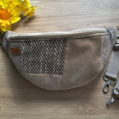 Beżowa nerka crossbody z teksturowaną siatką i panelami ze sztruksu oraz regulowanym paskiem na drewnianej powierzchni
